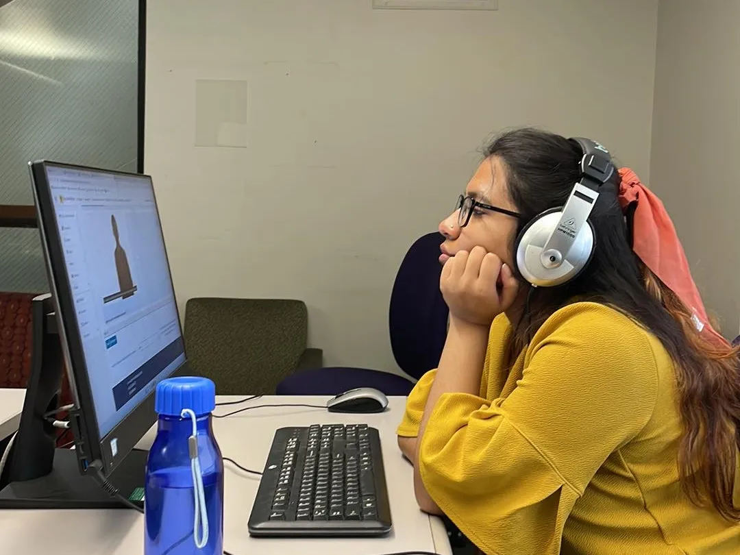 Noshin with headphones on working on a computer. 