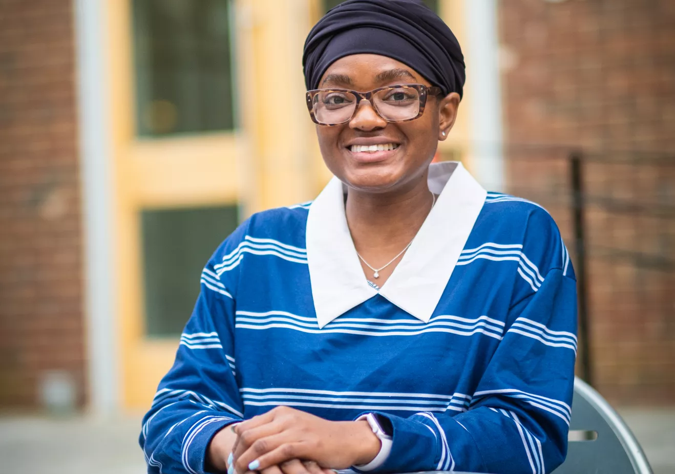 Saeina Charles smiling and seated at a table in front of the Enid Cook Center