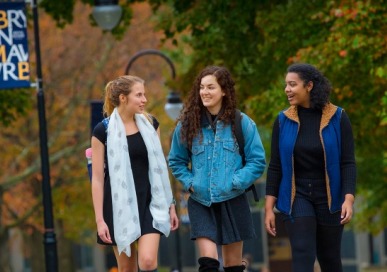 Three students walking on campus with a Bryn Mawr College flag in the background