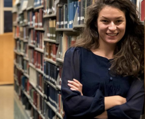 woman with long brown hair standing next to a row of bookcases