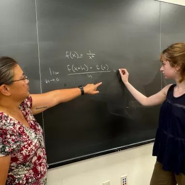 Two people at a chalkboard solving a math problem