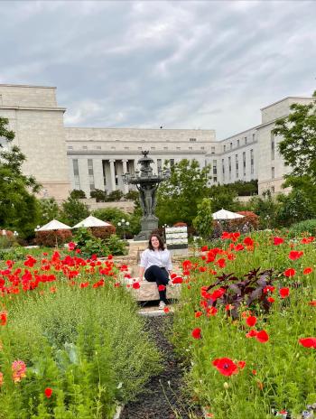 Zoe Balk seated outside amongst flowers with a building in the background