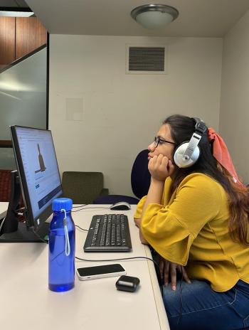 Noshin with headphones on working on a computer. 