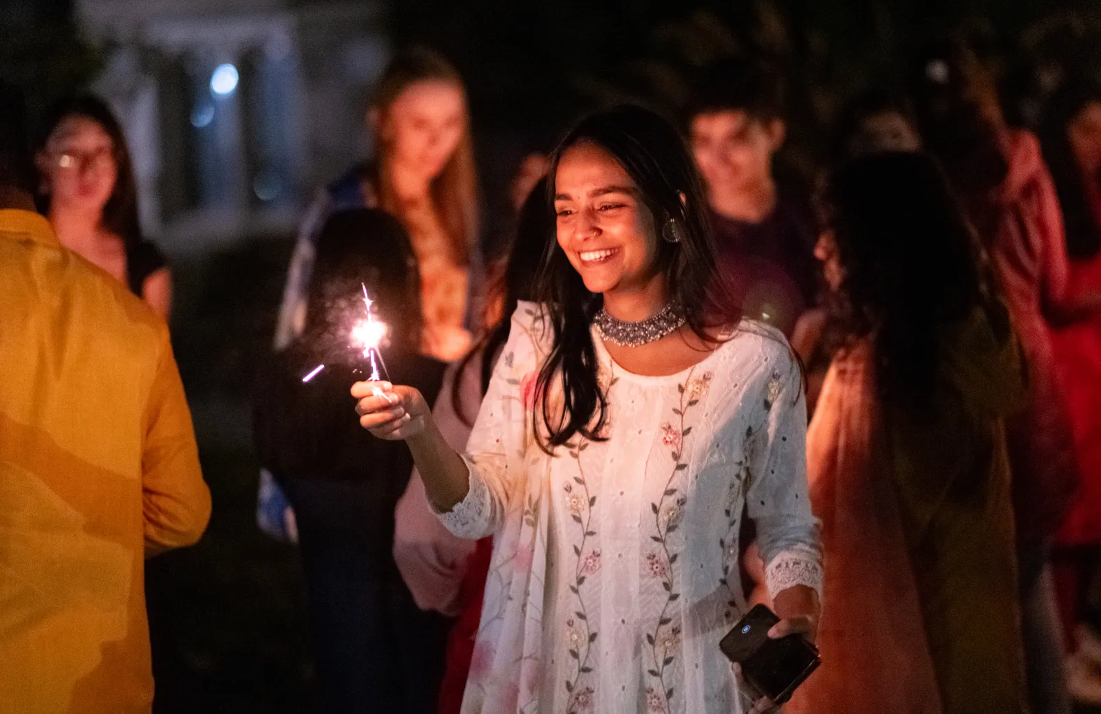 Group of smiling students at nighttime holding a sparkler