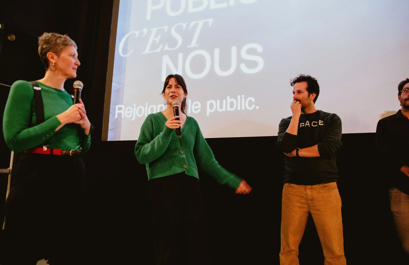 Gen, Aidan, and another participant listen stand on stage and listen to each other.