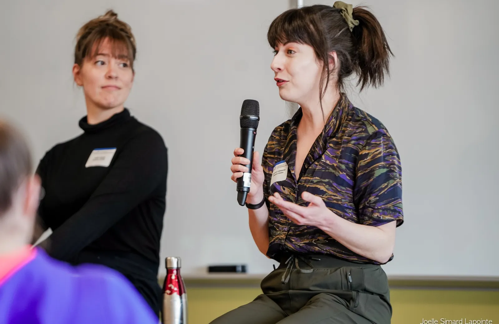 Geneviève Lamoureux holds a microphone and presents at the front of a room