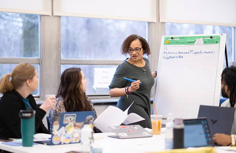 Woman at an easel with three students sitting in a NELI classroom