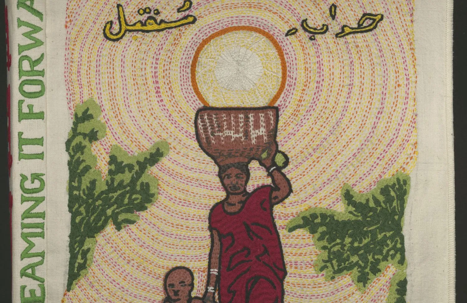 Cloth book with the words "Dreaming It Forward" stitched on the spine. The front image is a woman carrying a basket on her head while holding the hand of a child. There is Urdu text above her. 