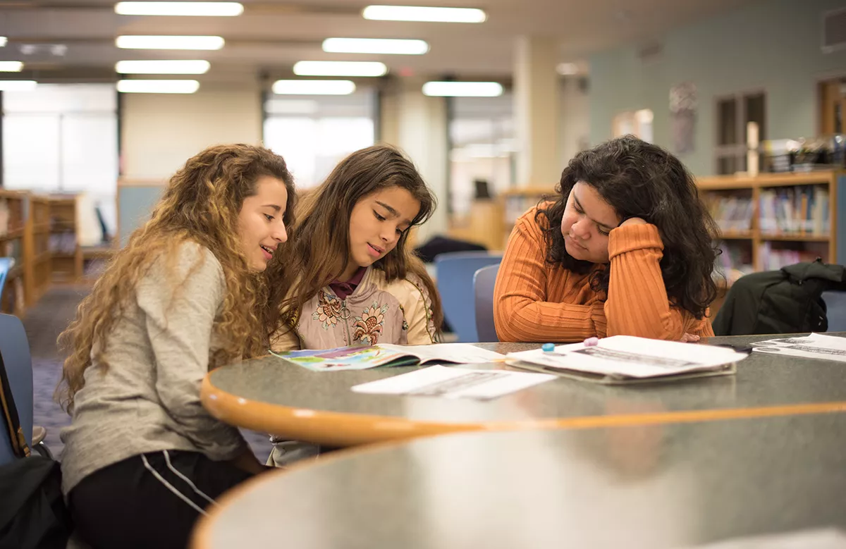 Zoila Regalado and Maria Vivanco pour over a book with a Willard Elementary School student in the school library.