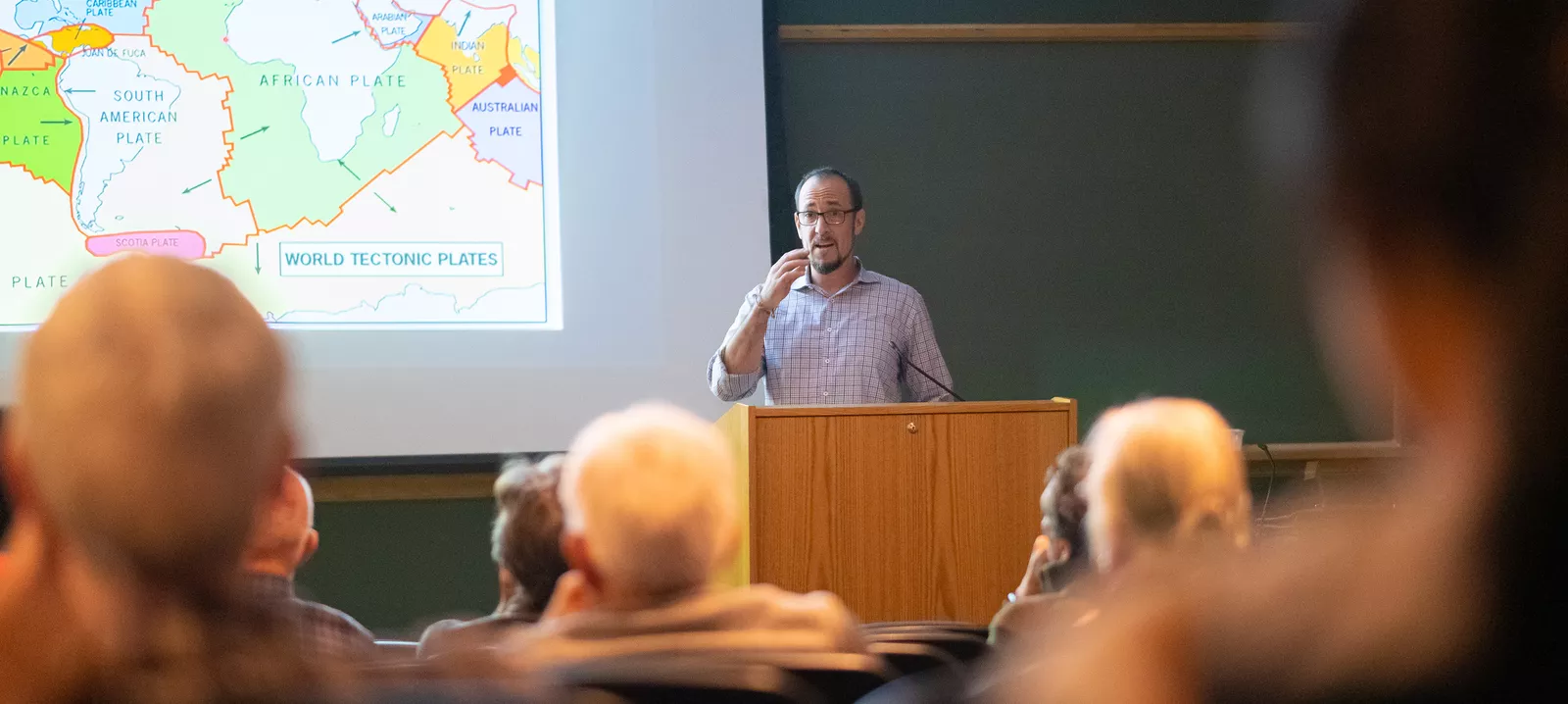 Professor next to map speaking to seated audience