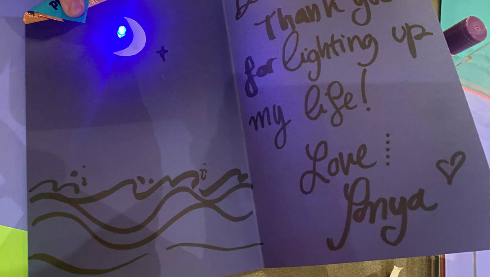 Electronic Valentine's Day card created during student workshop. The card is purple with black writing on the right flap and says, "Dear Mom, Thanks for lighting up my life. - Love, Janya." and has a blue light and the left flap