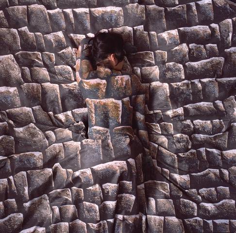 Cecilia Paredes painted to match wall of stones against which she leans.