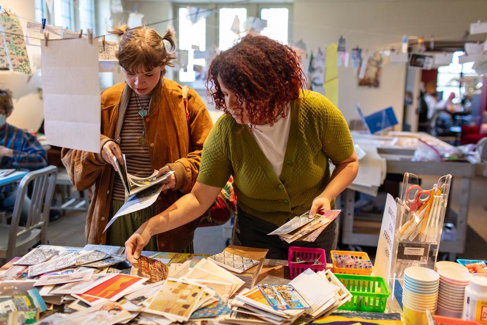 Two students look through collage supplies to make the fragments they will add to the collage