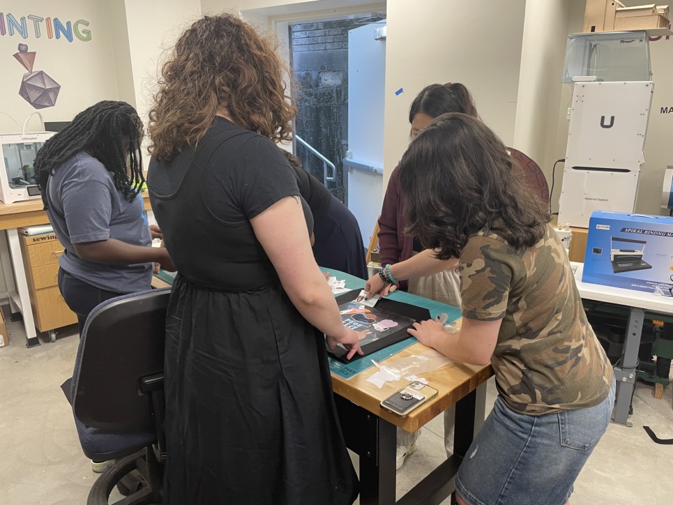 The 2024 DTI's work with Bronwen Densmore, Makerspace Coordinator, on an introductory project, creating a group tote bag.