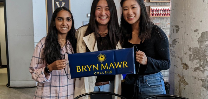 Three GOLD alums pose with a blue banner that says Bryn Mawr College.