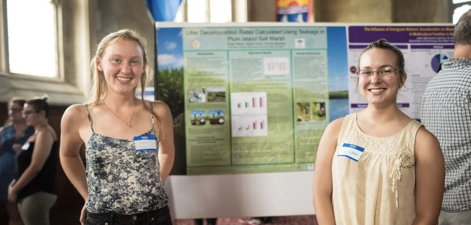Two students smiling in front of a research poster in the Great Hall