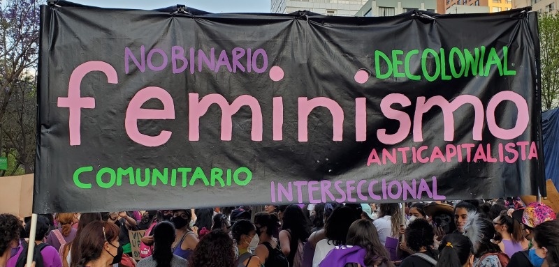 hand-painted banner reading "feminismo" held by women at an outdoor march