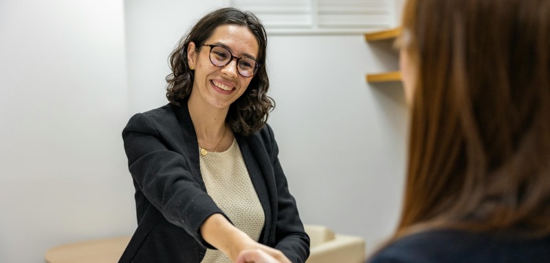 Two people shaking hands while sitting across from one another at a table.