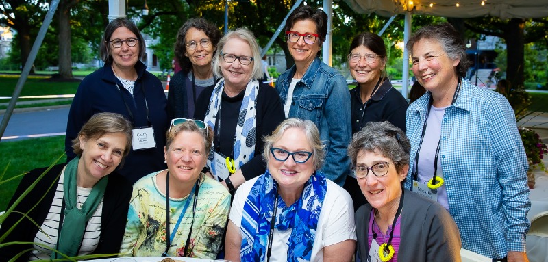 A group of women, some sitting, some standing, smile at the camera.