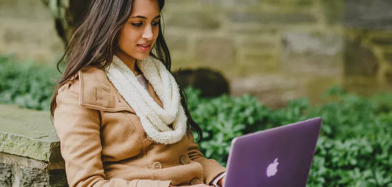 Student sits outside looking at computer