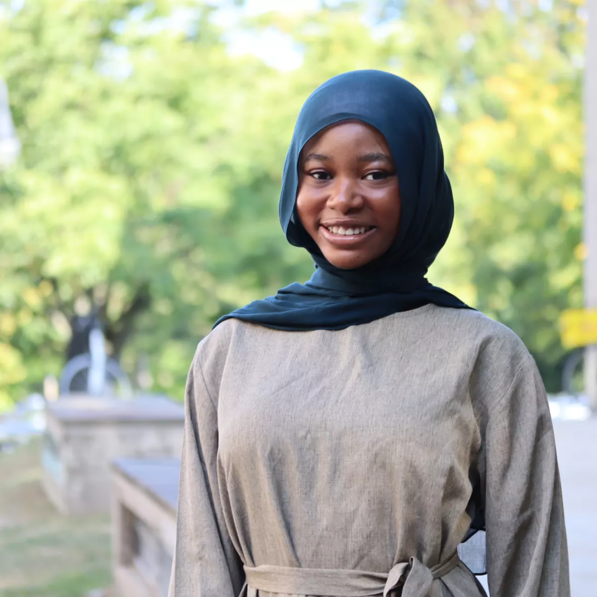 Faiqah in a tan dress and green scarf.