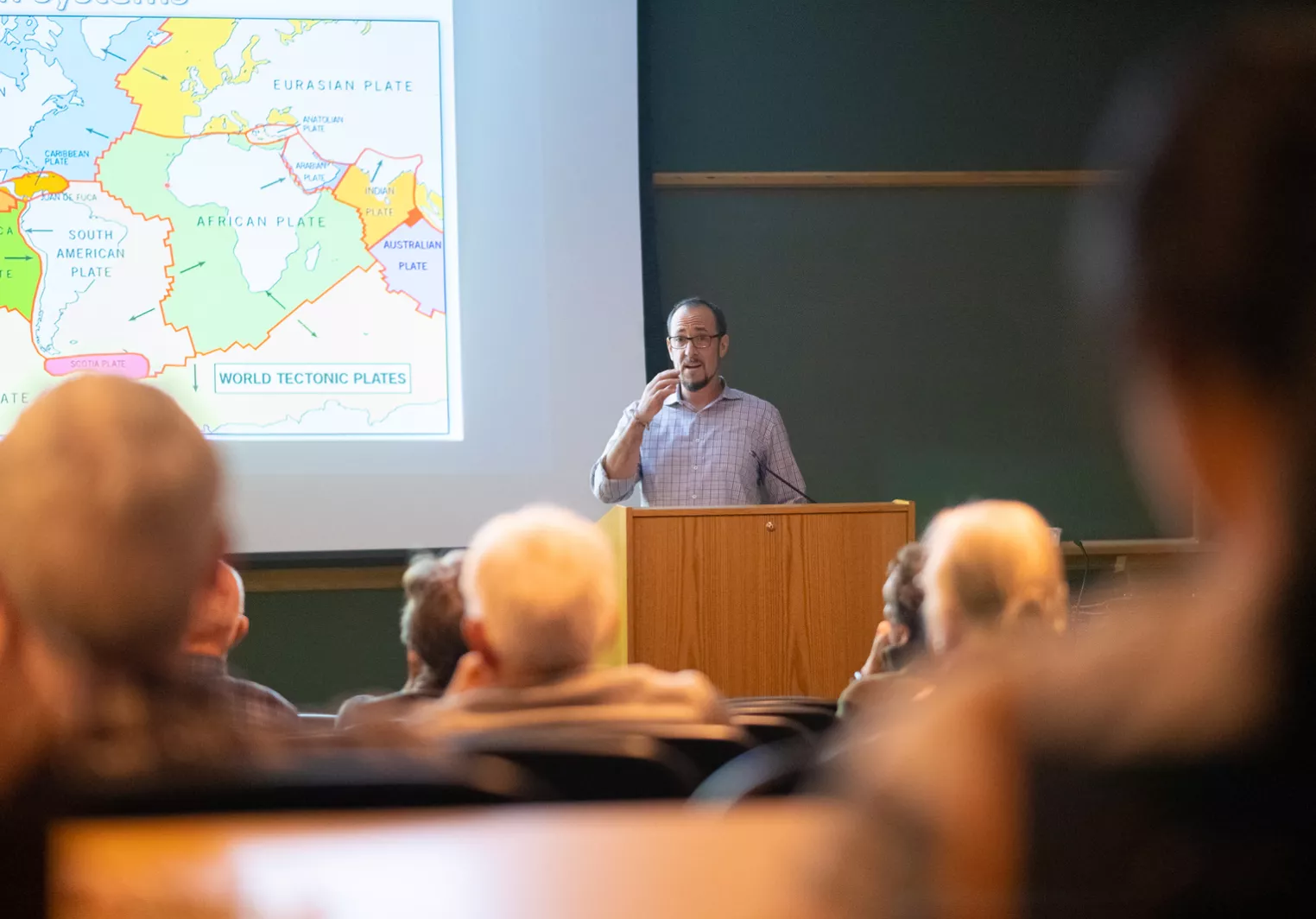 Professor next to map speaking to seated audience