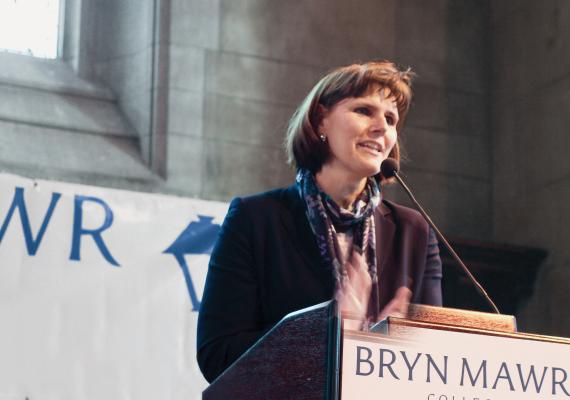 Kim Cassidy standing behind a podium with a Bryn Mawr banner in the background