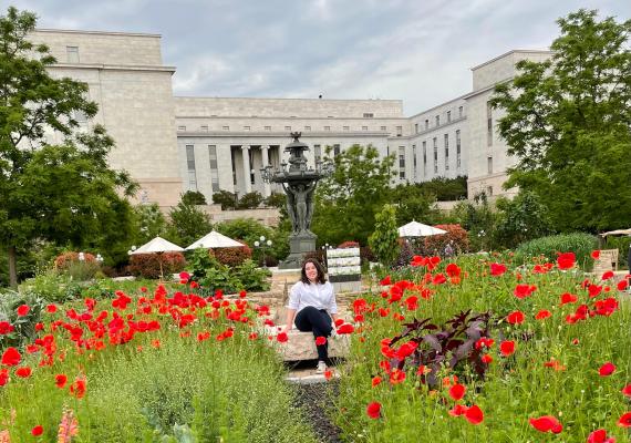 Zoe Balk seated outside amongst flowers with a building in the background