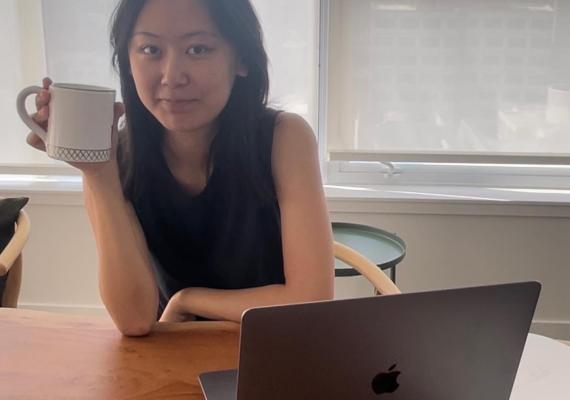 Ashley in front of a laptop holding a mug. 