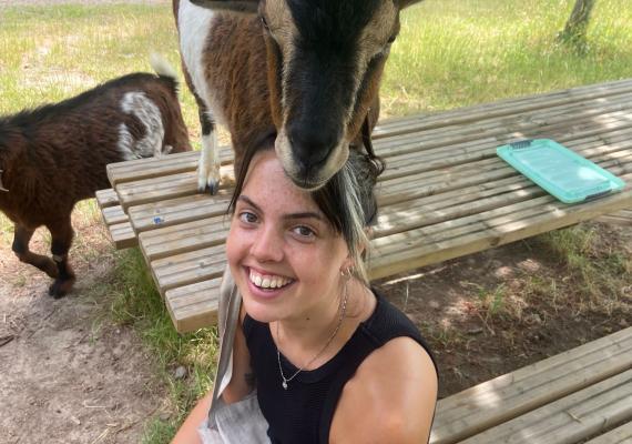 Clara Grosse sitting and smiling amongst goats. 