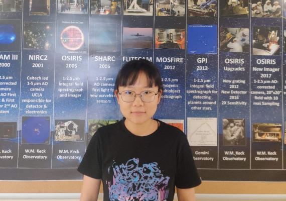 Xiyue Shen standing in front of a UCLA poster. 