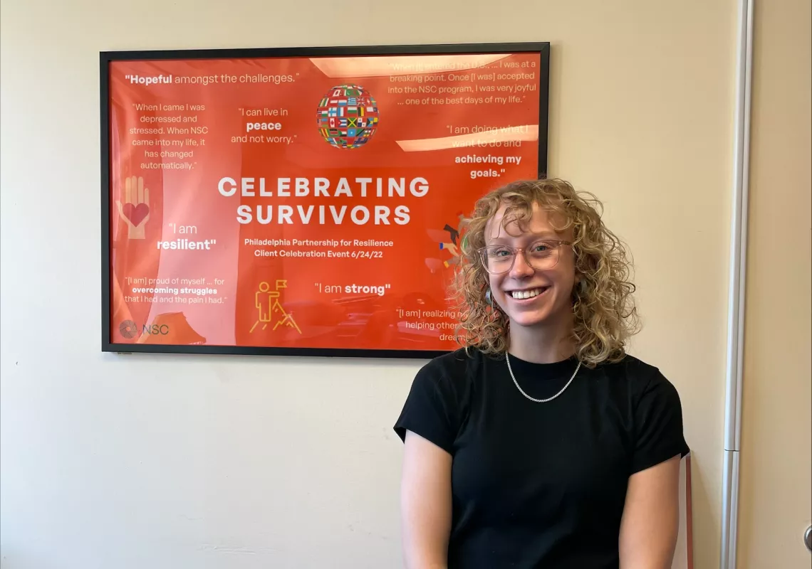 Emma Gross '25 poses in front of a "celebrating survivors" poster