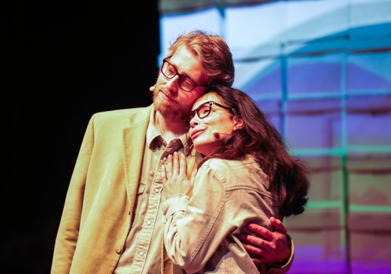 Two actors embrace in front of colorful screen