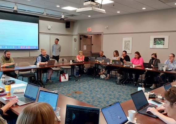 A room full of people with laptops listening to a speaker