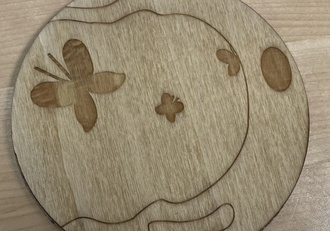 Wooden coaster created during a workshop on laser cutting. The design has a butterfly to the left and a wave to the right.