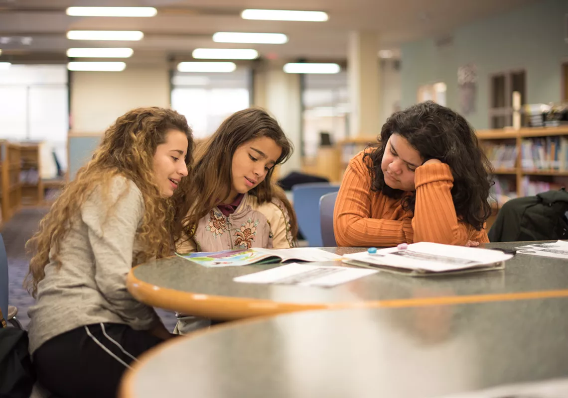 Zoila Regalado and Maria Vivanco pour over a book with a Willard Elementary School student in the school library.