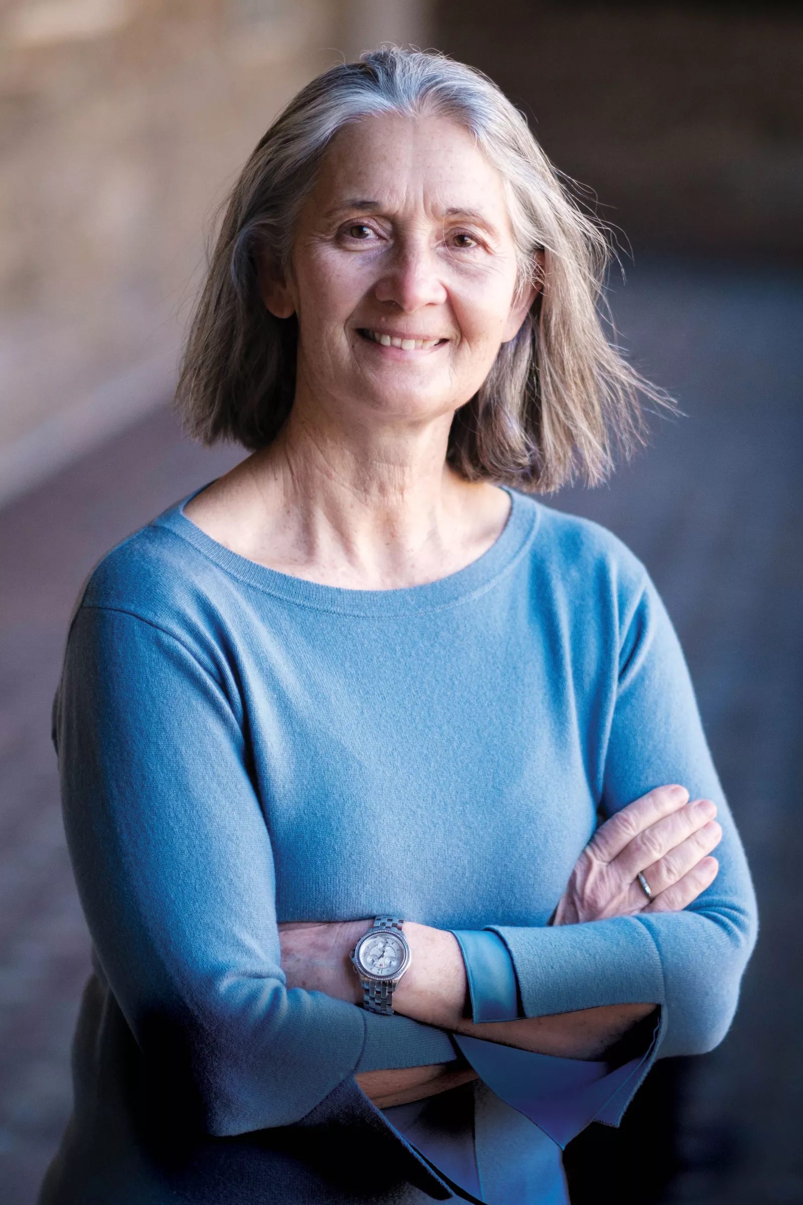 Kathy Tierney stands with arms crossed, smiling, wearing a blue shirt