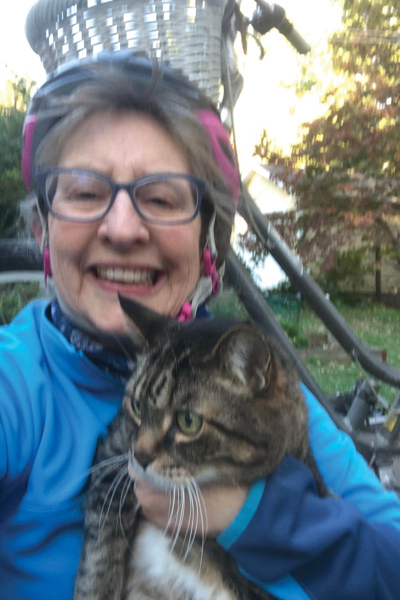 Portrait of Susan Burt wearing a bike helmet and holding a tabby cat.