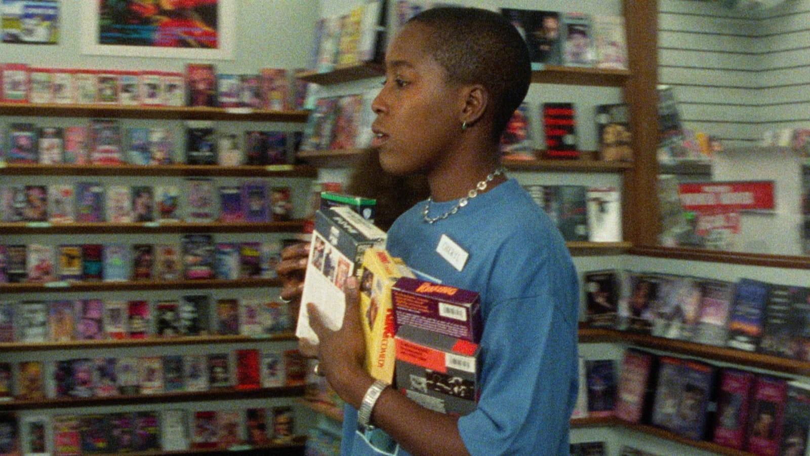 A woman walks through a video store holding a stack of VHS tapes